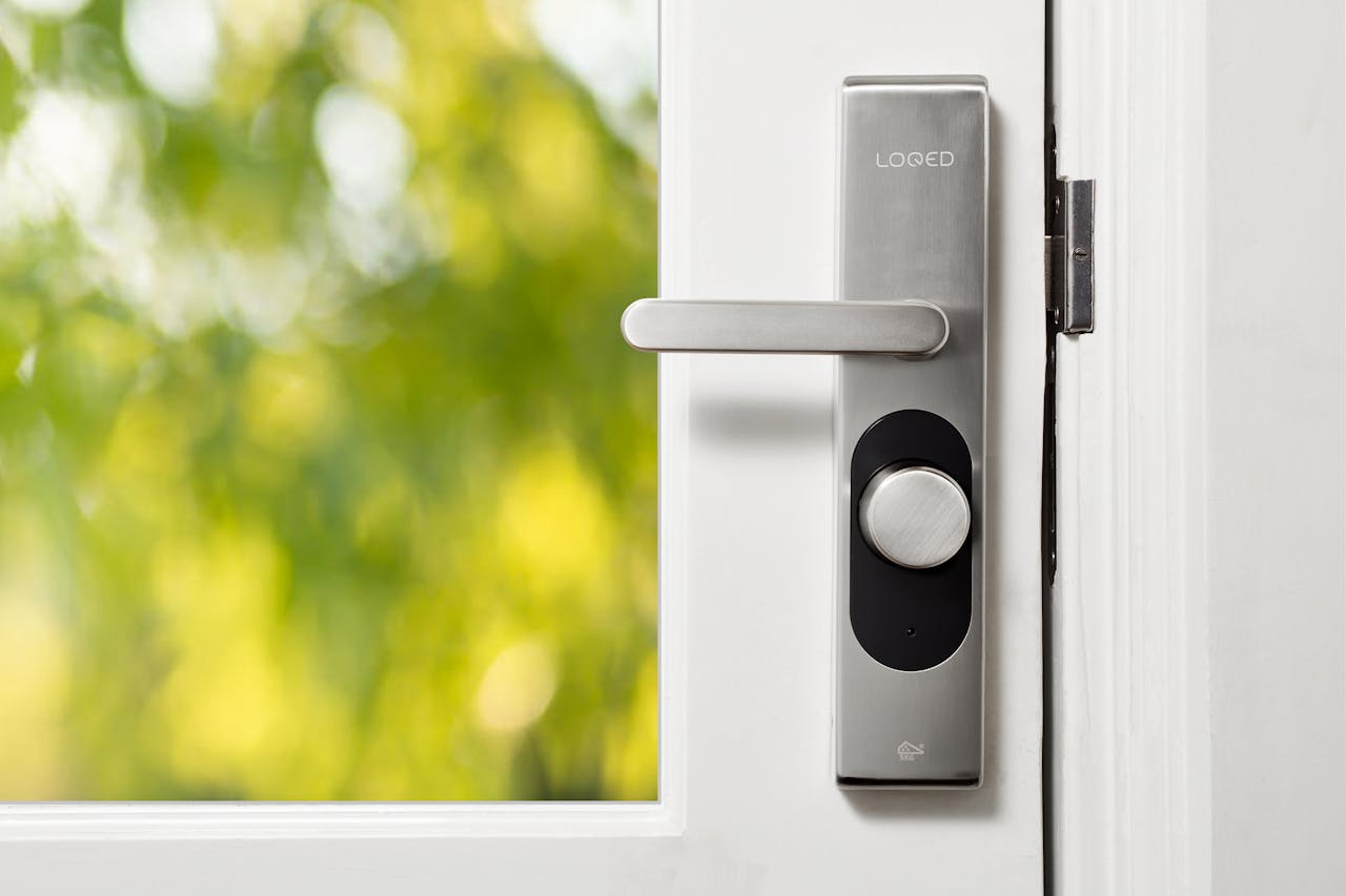 Sleek smart door lock on a white door with blurred green foliage in the background.